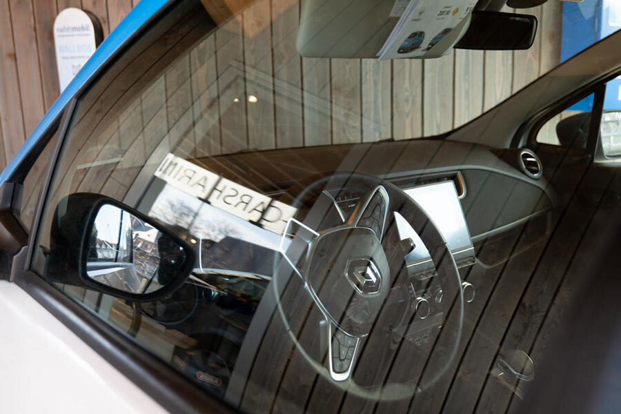 Ein Foto eines Elektroautos der Marke Renault. Durch die Fensterscheibe der Fahrertür ist das Lenkrad und die Mittelkonsole des Fahrzeugs zu sehen. 